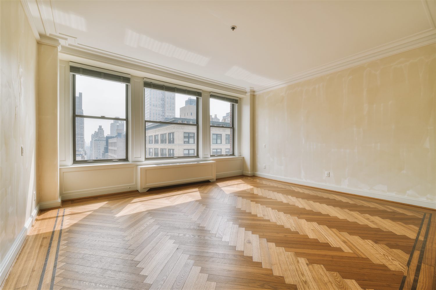 Pre-war apartment living room with herringbone floors, tall windows and a view of Manhattan buildings
