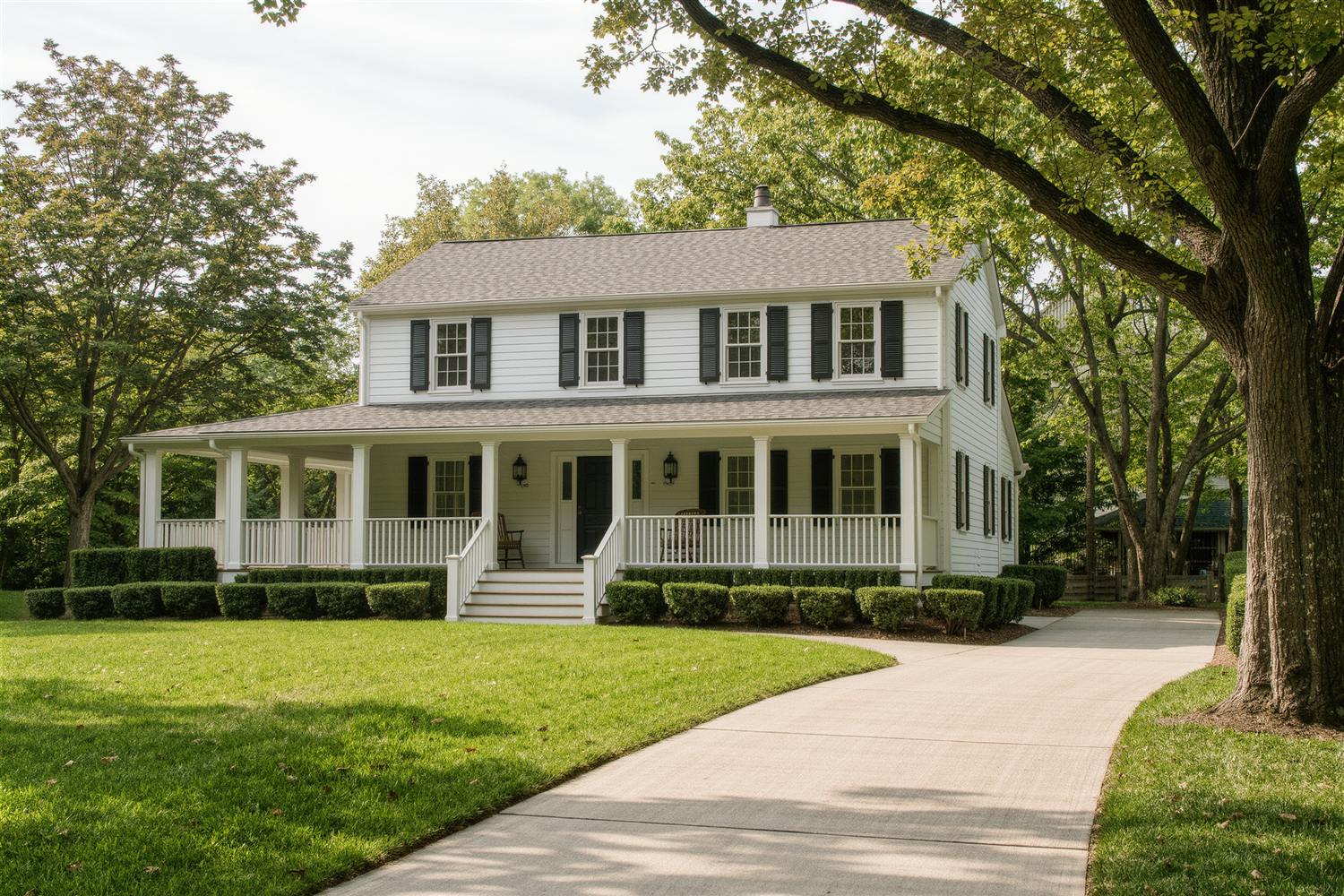 Detached two-story house with white siding, dark shutters, a front porch and a curving driveway under mature trees