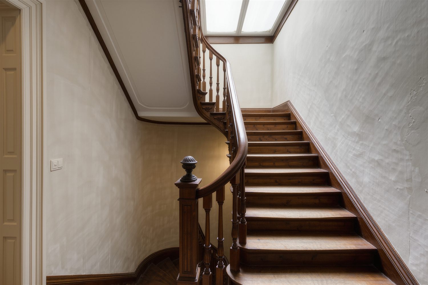 Wooden staircase with a turned newel post and balusters rising under a skylight in a row house stair hall